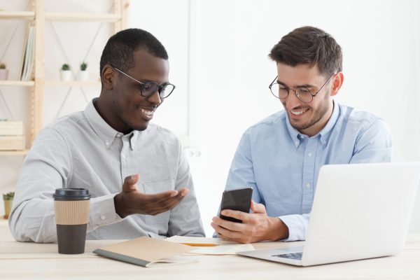 One colleague helping another with task showing solution on smartphone at office desk